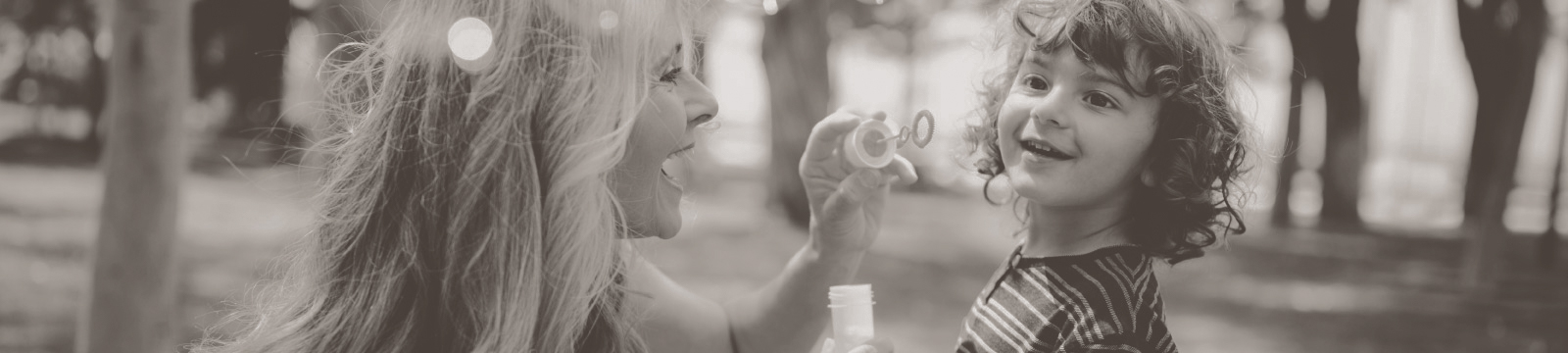 Woman blows bubbles for young child in a park.